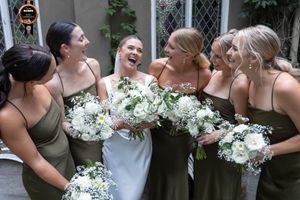 Bride laughing out loud surrounded by her five bridesmaids all holding their white bouquets