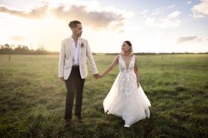 Bride and Groom holding hands in a field with their backs to golden setting sunlight
