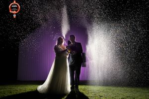 Groom and bride spray lots of champagne around them with back lighting and purple shed