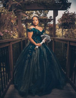 Full-length portrait in emerald ball gown on wooden bridge outdoors.