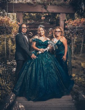 A formal group pose in an outdoor garden setting with a sparkling teal ballgown as the centerpiece.