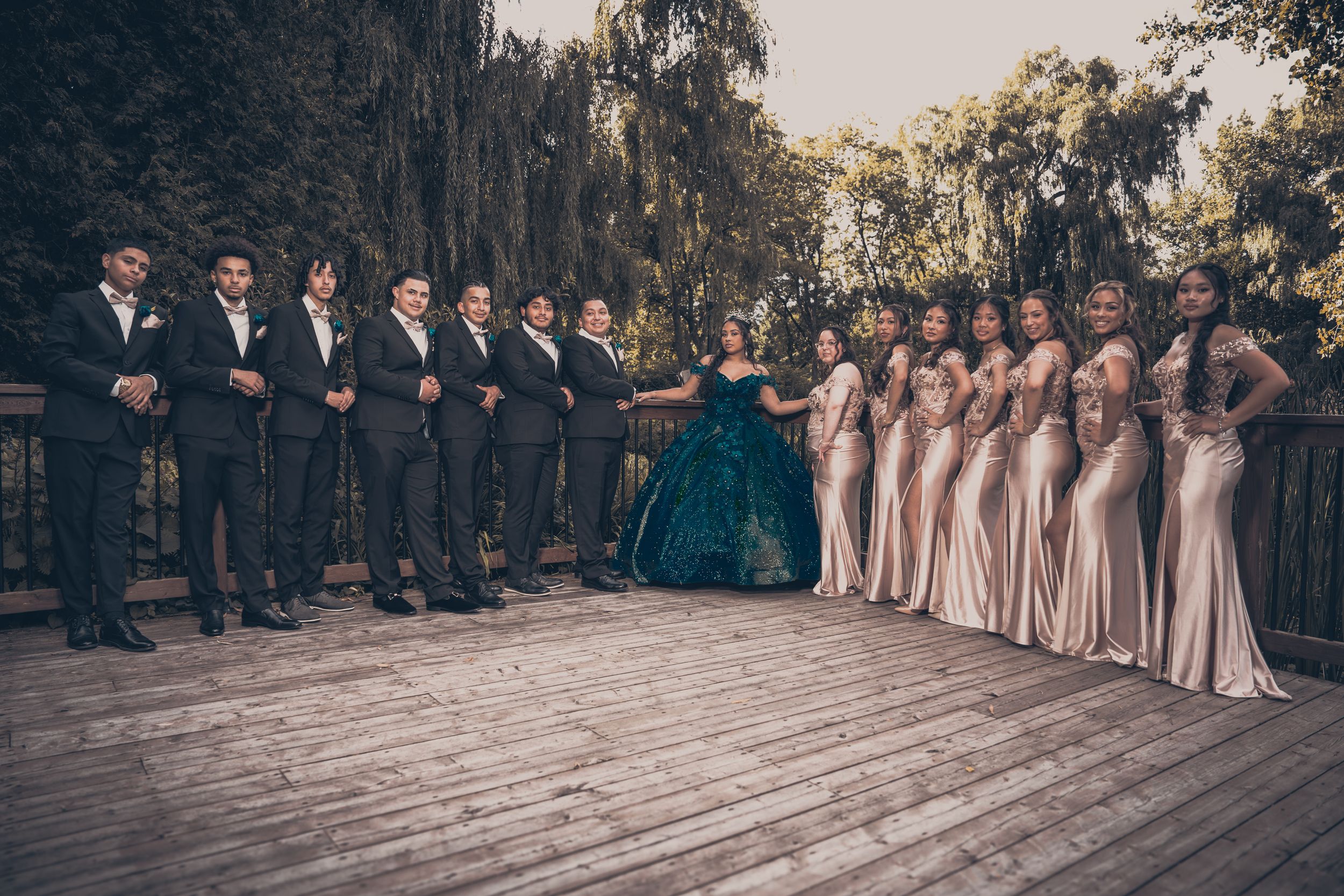 A formal wedding party lined up outdoors with bridesmaids in blush and groomsmen in dark suits.