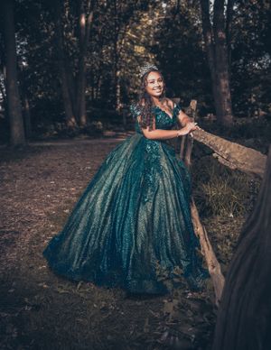A stunning teal ballgown photographed in a moody forest setting.