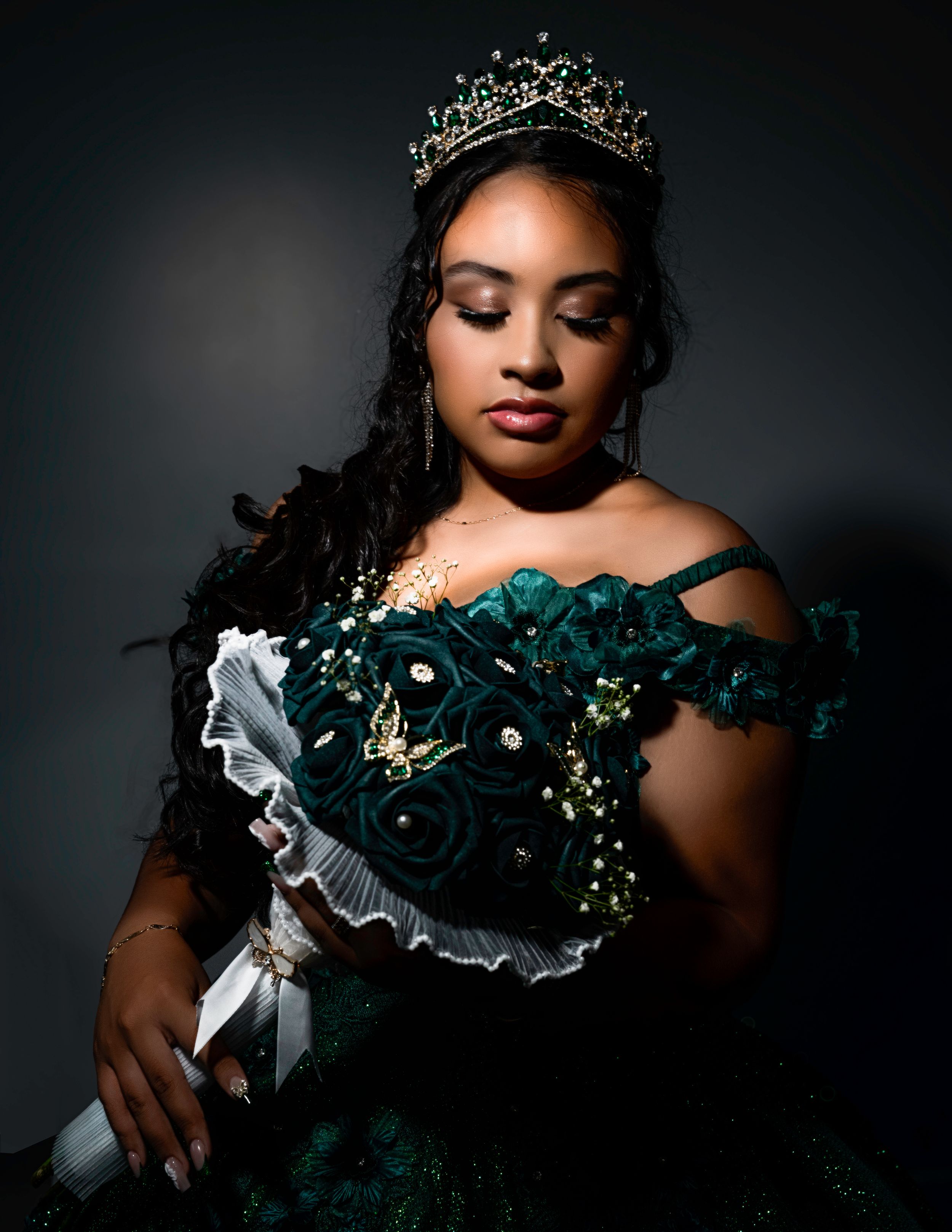 Elegant portrait in emerald gown with tiara and floral bouquet against dark background.