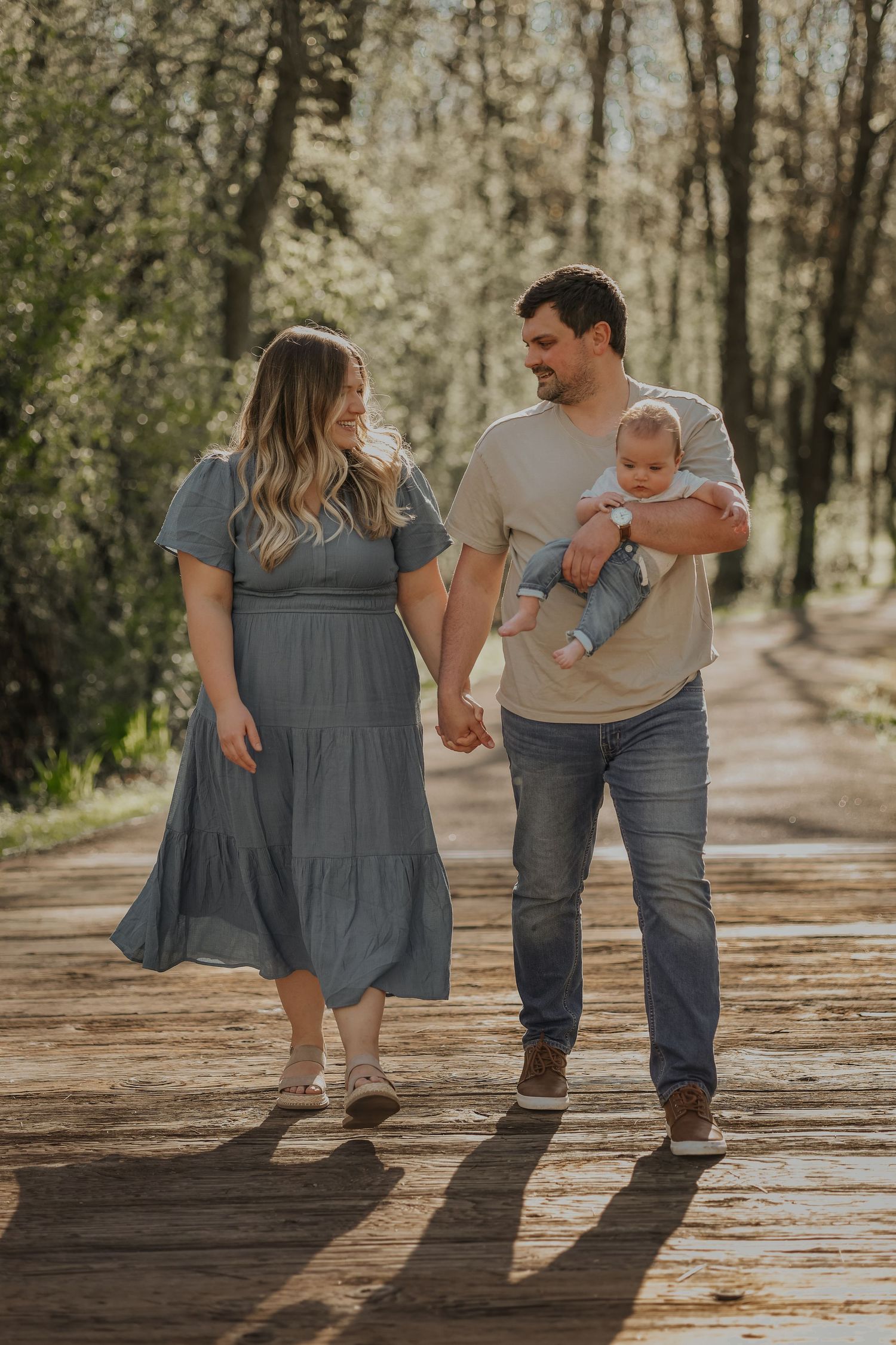 A family walks together holding hands on a wooden boardwalk through a forest.