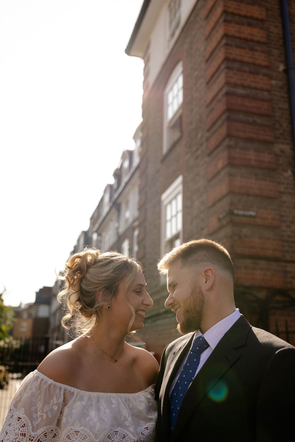 A bride and groom share intimate moments in a series of photos against a brick building with sunlit windows.