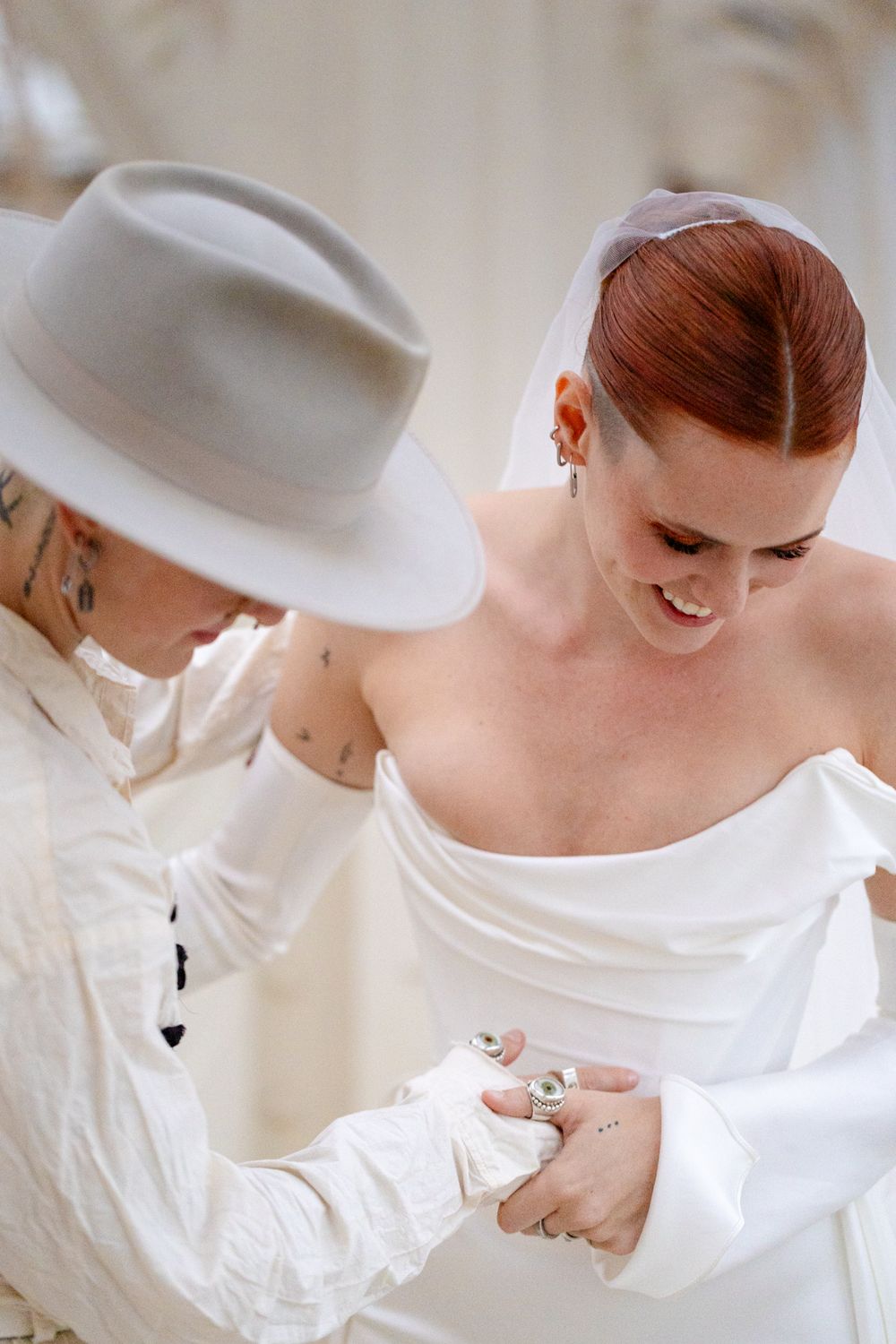 A tender moment during wedding preparations as final adjustments are made to a white bridal gown.