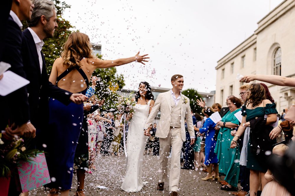 Newlyweds walk through a shower of confetti outside a church while wedding guests celebrate their joyful exit.