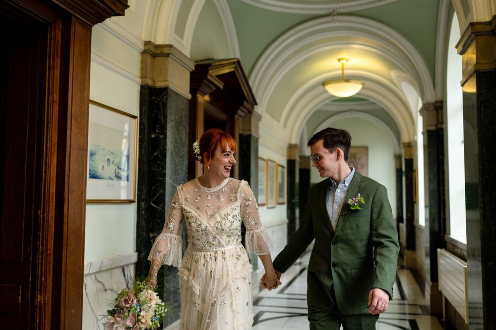 A bride and groom share an intimate moment in an elegant hallway with ornate architectural details and warm lighting.
