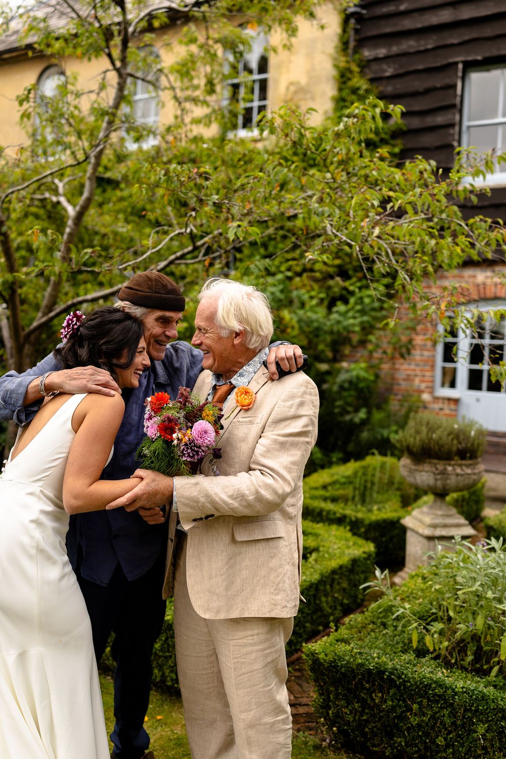 A tender moment shared between loved ones in a garden setting with lush greenery and a rustic house exterior.