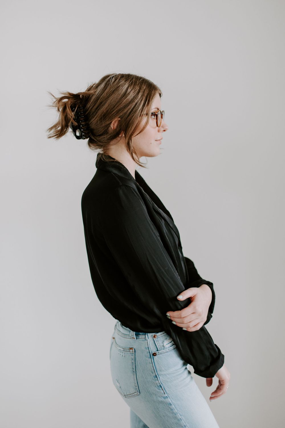 Side profile of person in black sweater and jeans standing against white wall.