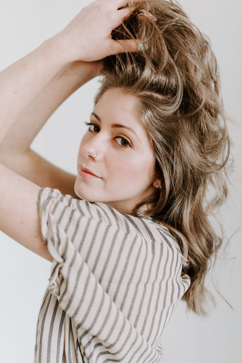 Portrait of someone in a striped shirt with tousled brown hair against a light background.