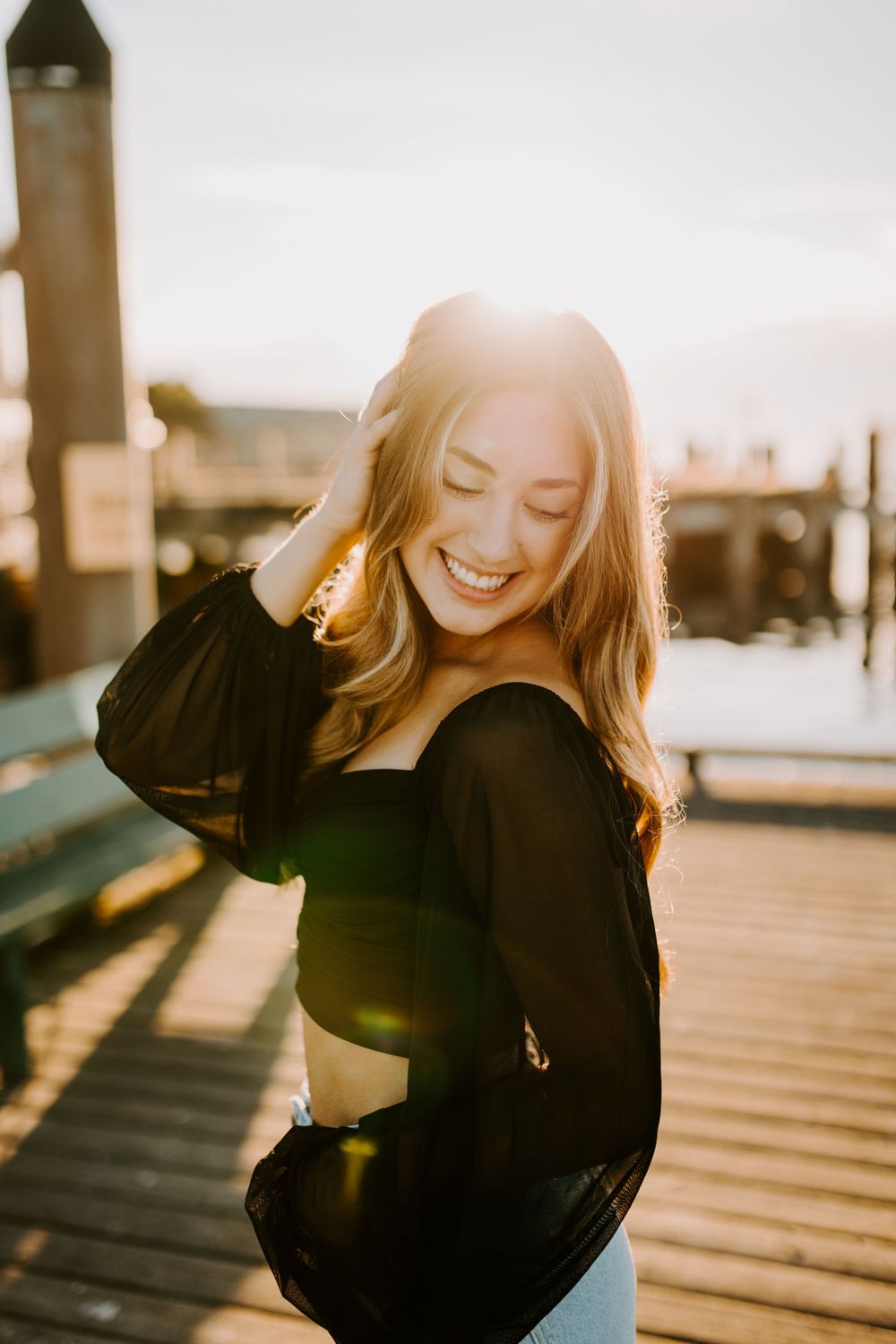 Candid sunset portrait on wooden dock with water and boats in background.