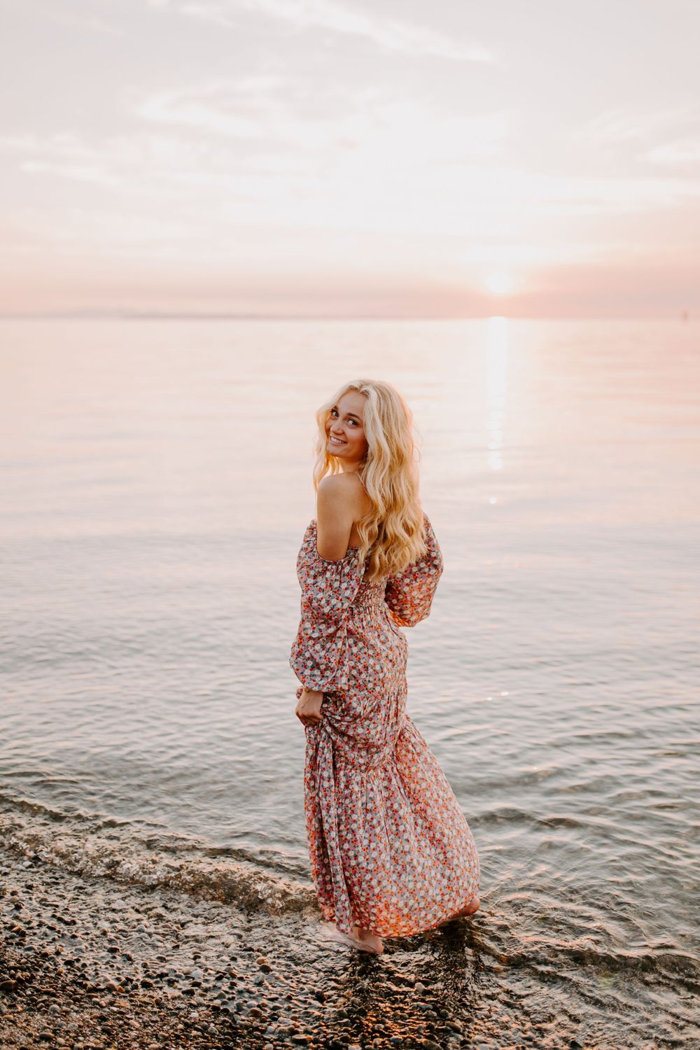 Sunset beach portrait with flowing floral dress against pink sky.