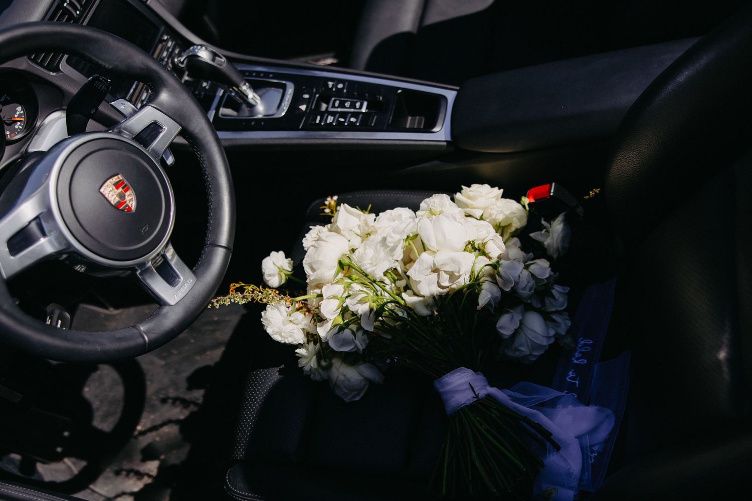 Wedding bouquet rests on leather seats inside a Porsche luxury car interior.