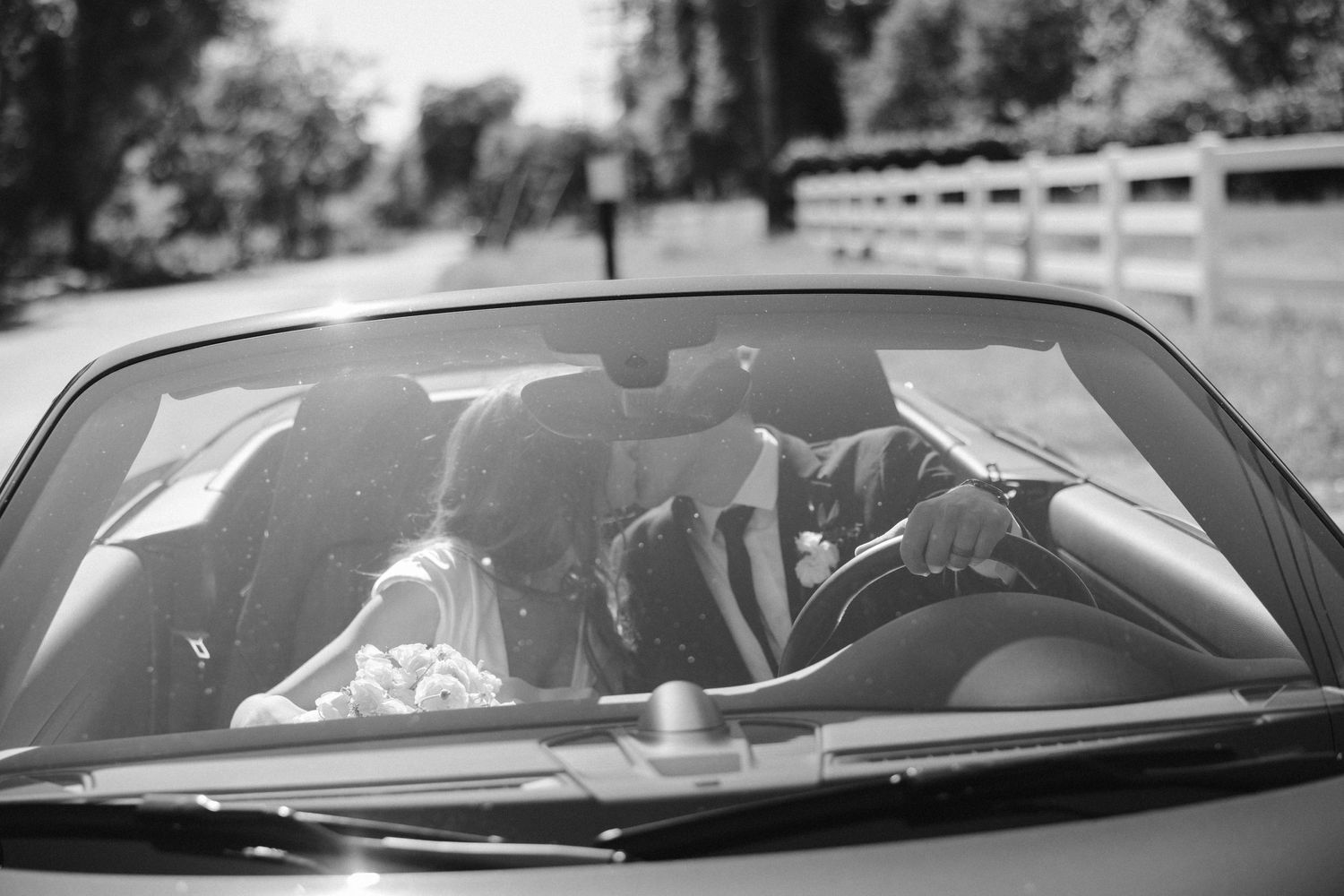 Artistic black and white photo through windshield of couple in convertible car.