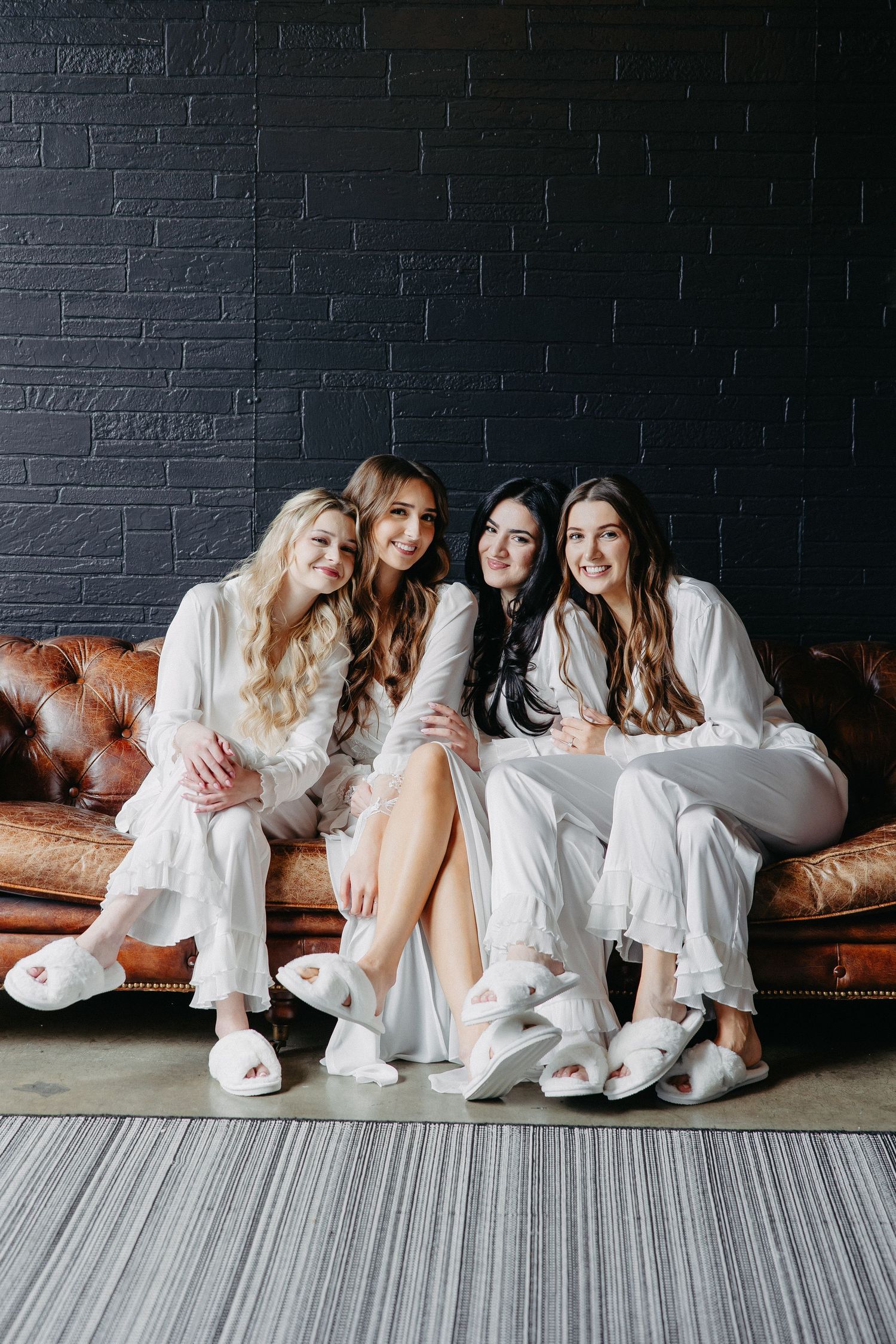 Group wearing matching white loungewear sits together on brown leather couch against dark wall.