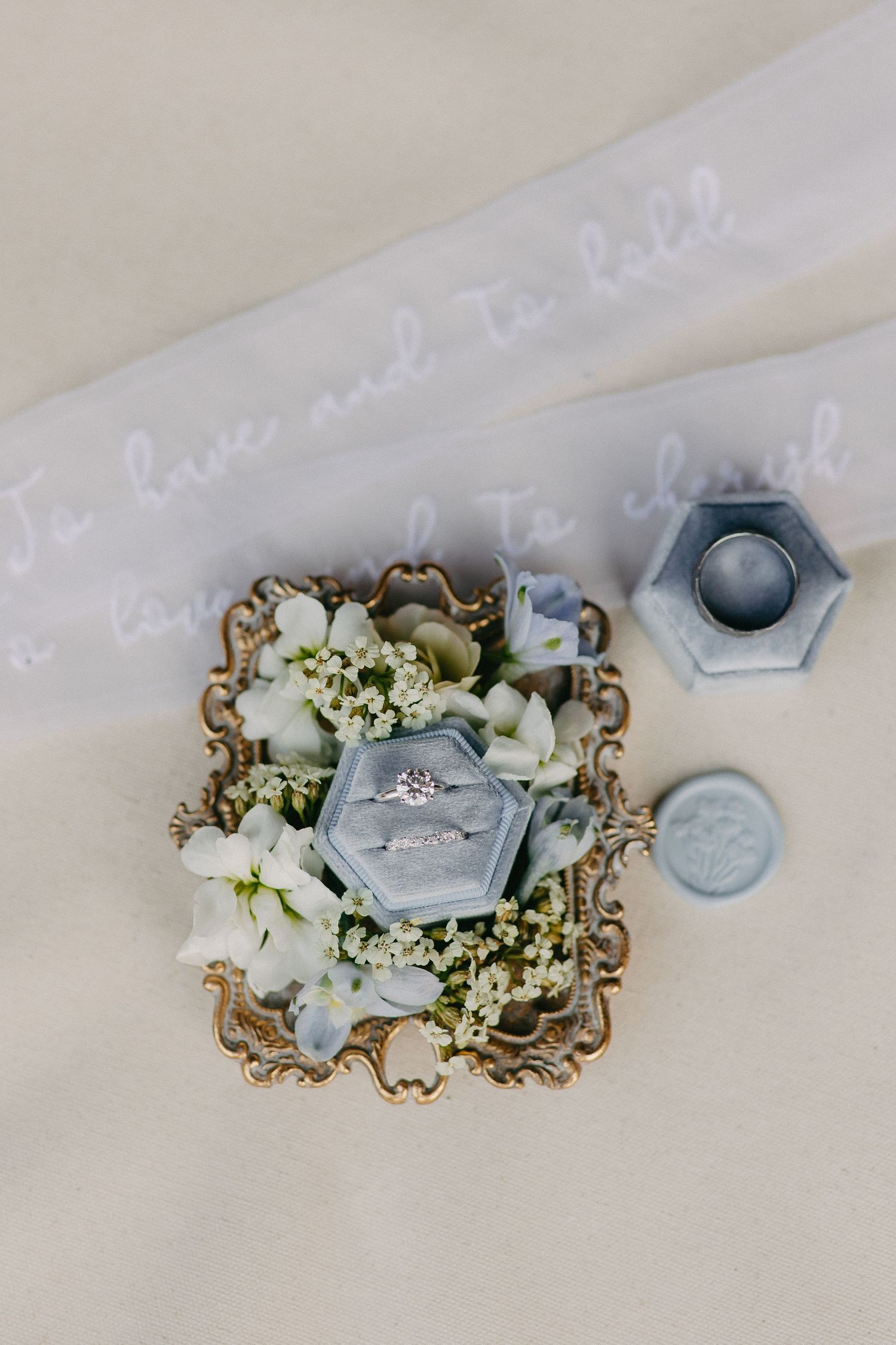Wedding ring displayed in hexagonal box with white flowers on ornate tray.