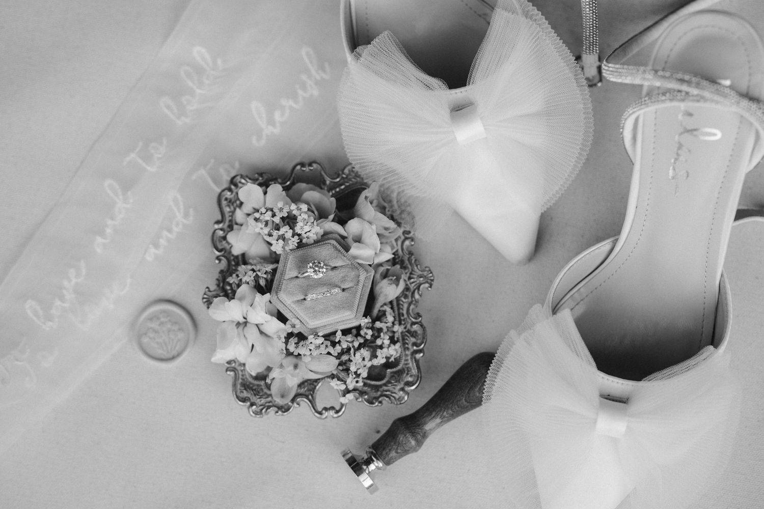 Black and white photo of wedding details with rings and floral arrangements.