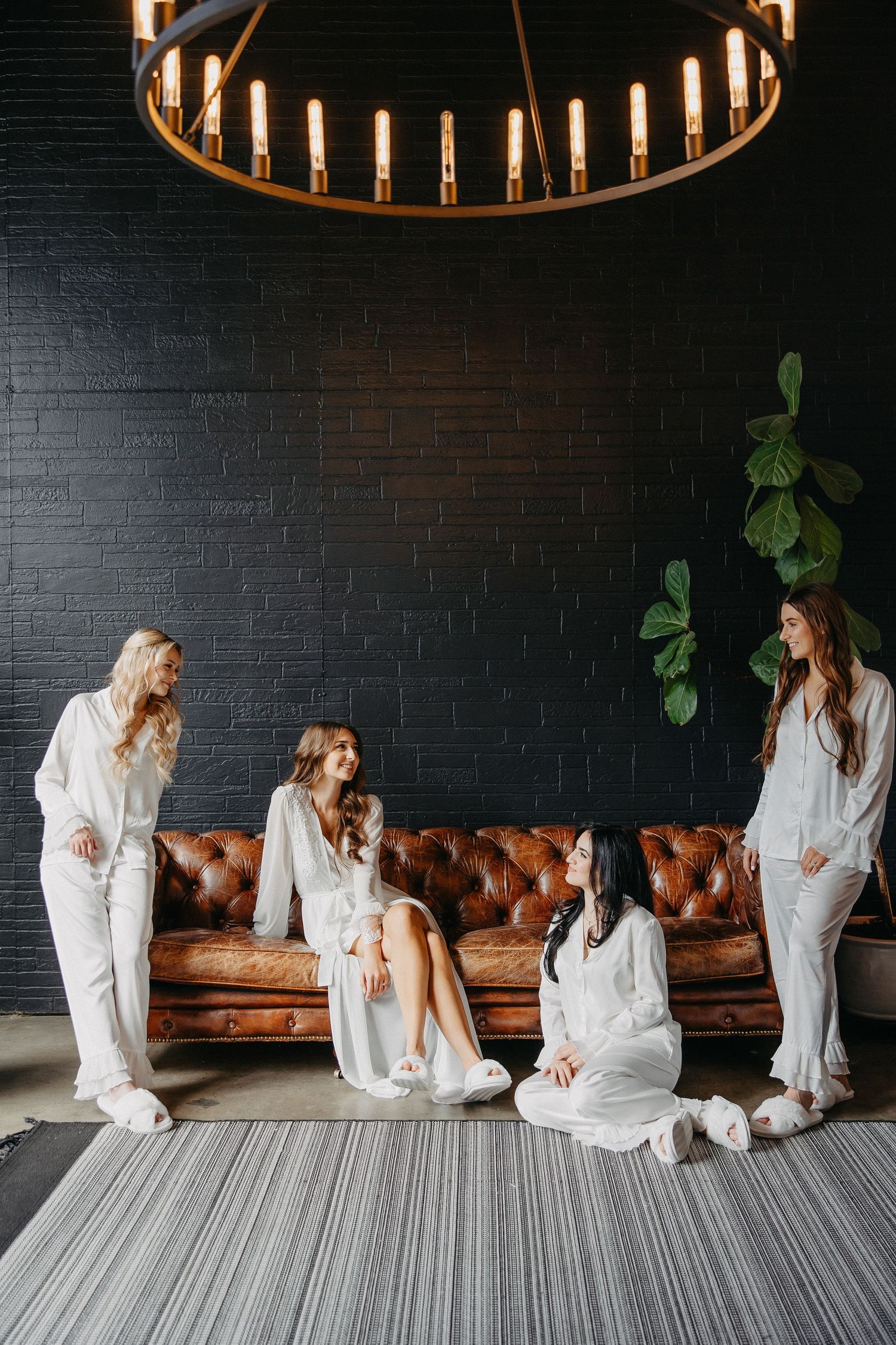 White-clad group lounging on brown leather couch under circular chandelier in modern space.