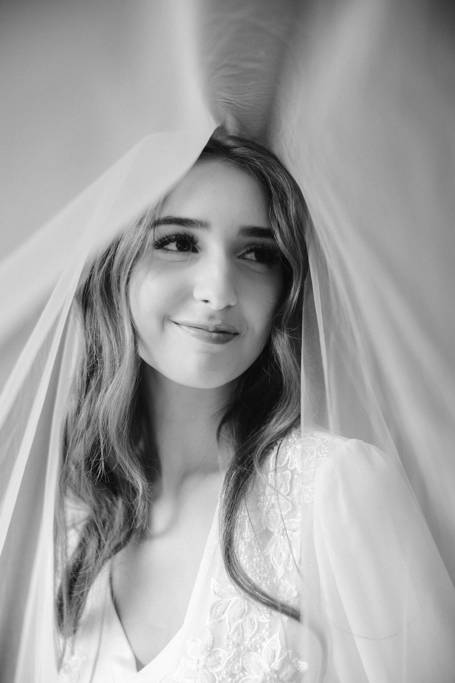 Close-up bridal portrait with sheer veil and gentle smile in black and white.