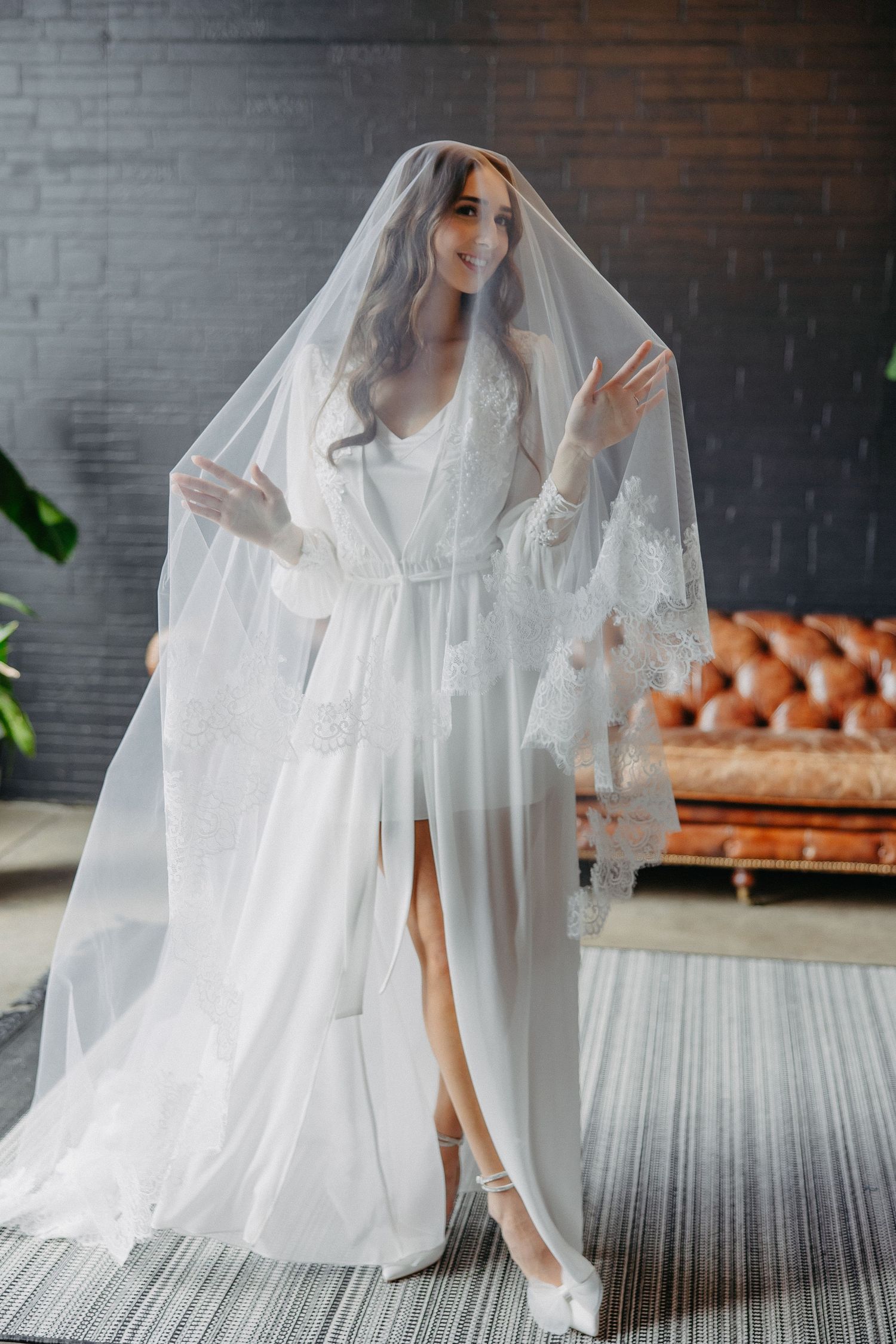 Bridal boudoir photo with flowing white robe and long veil in modern industrial setting.
