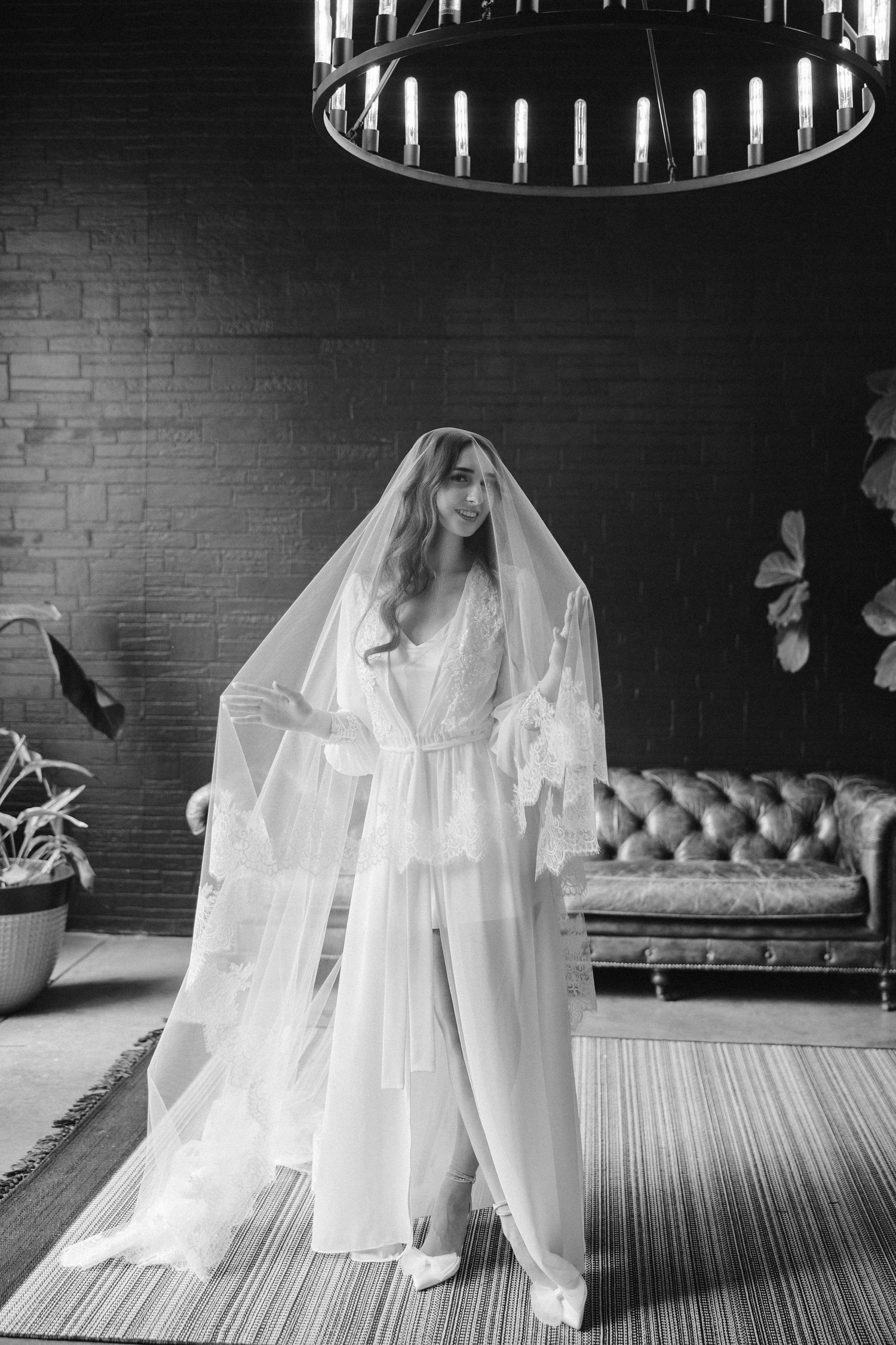 Dramatic black and white bridal pose under chandelier wearing flowing robe and veil.
