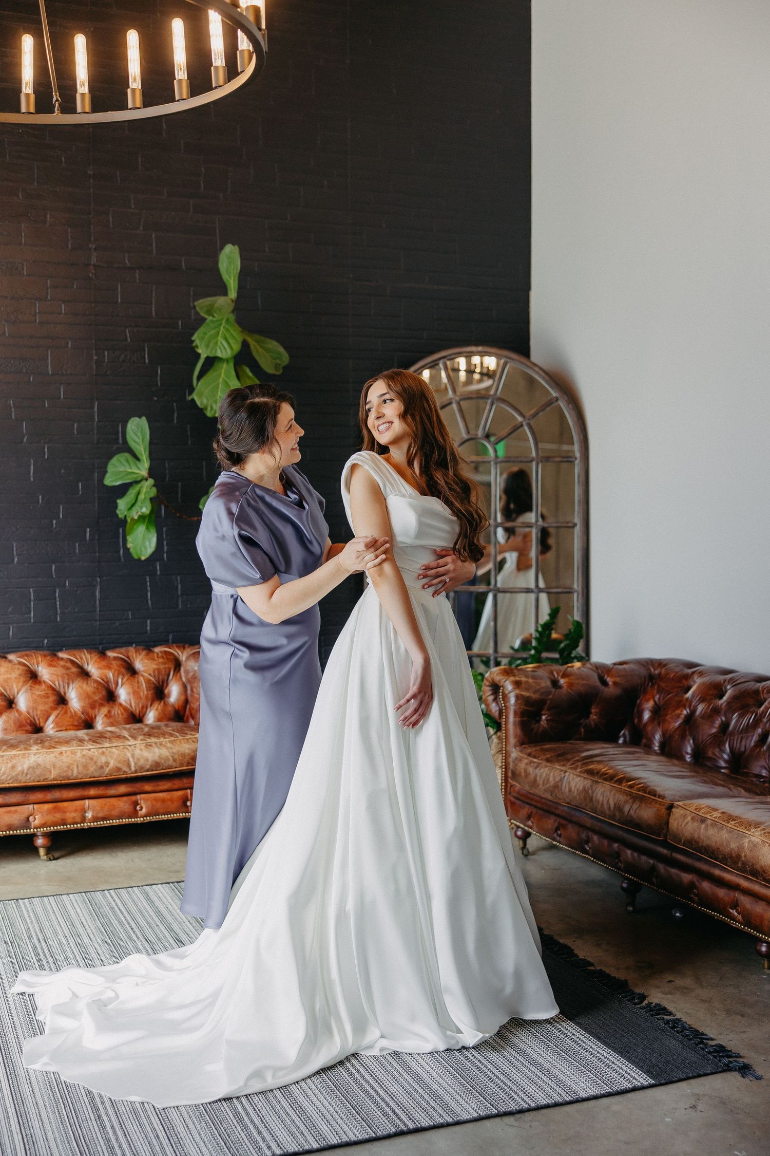 A wedding dress fitting session in an elegant room with vintage leather sofas and modern lighting.