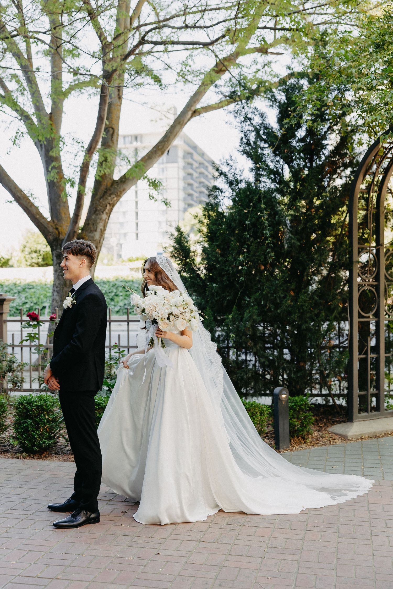 A wedding couple poses in a garden setting with brick pathways and iron gates.