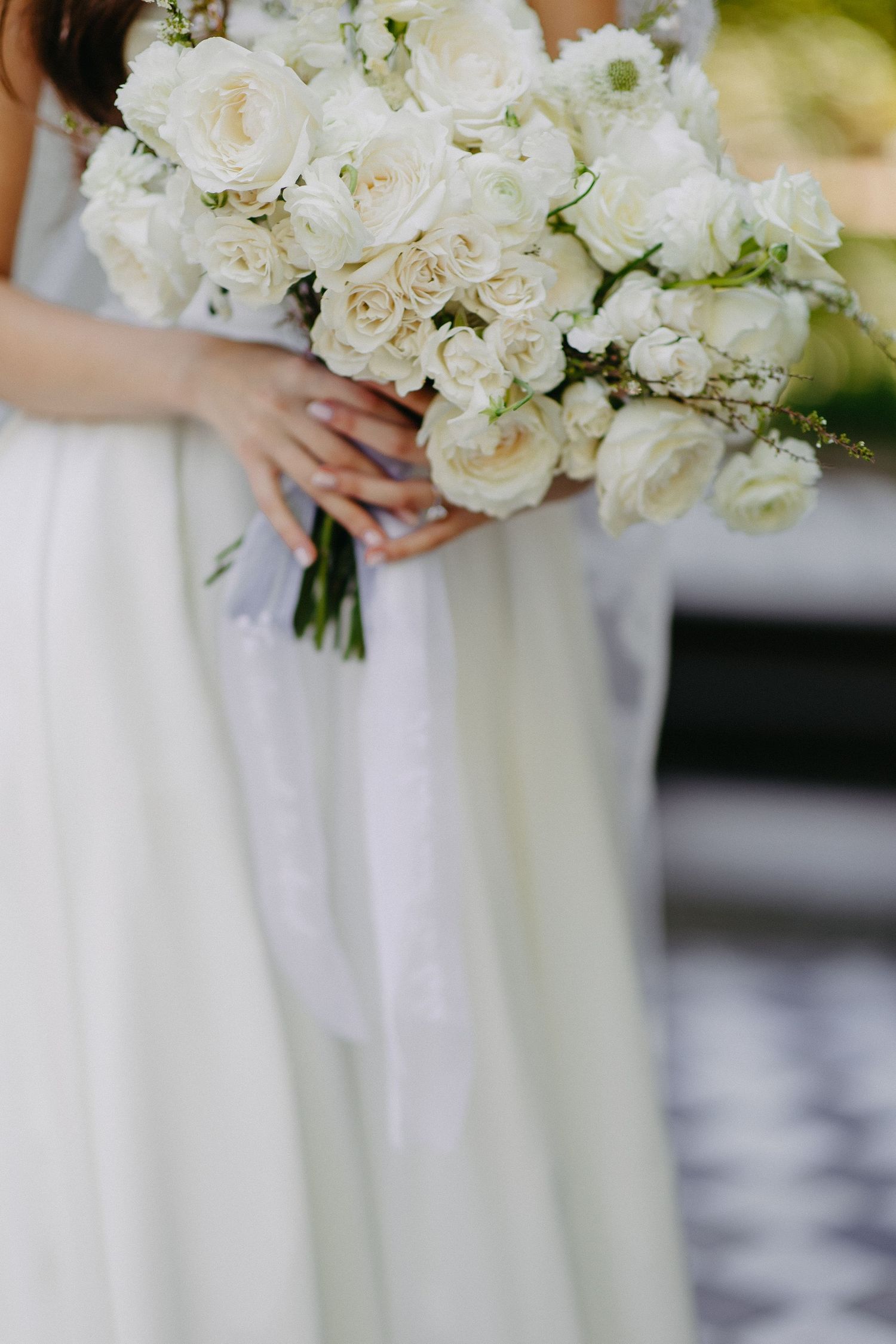 Close-up of white rose wedding bouquet held against flowing bridal gown.