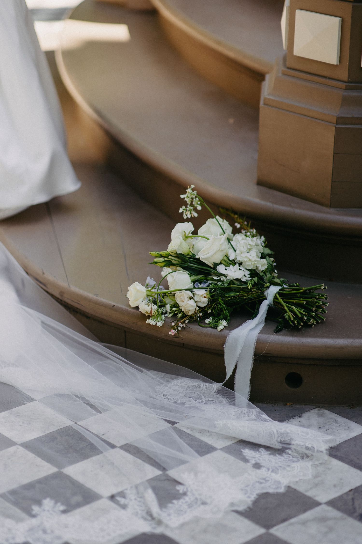 White wedding bouquet with roses and greenery rests on a checkered floor.