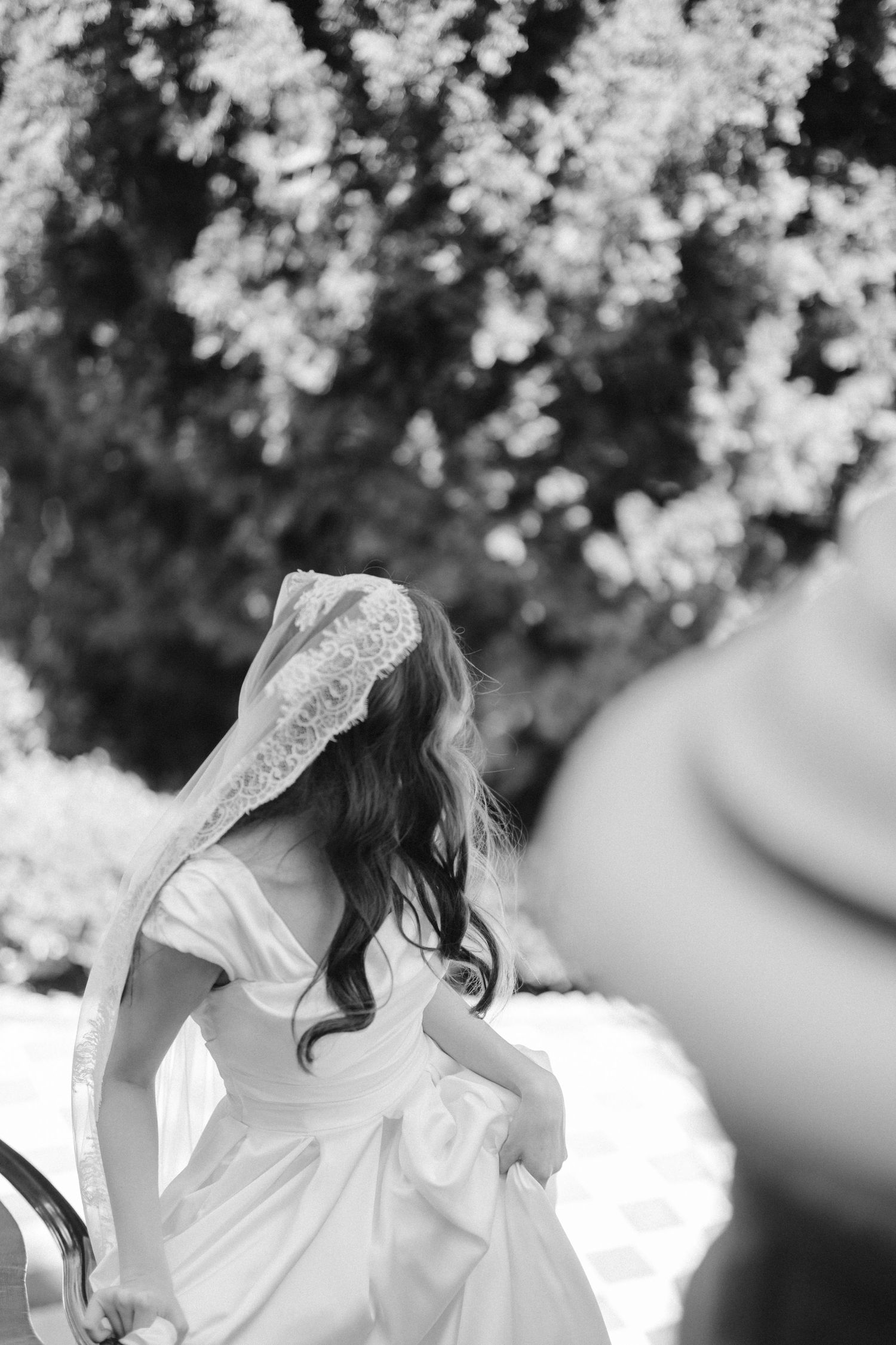 Black and white photo of a bride in a flowing dress with a veil outdoors.