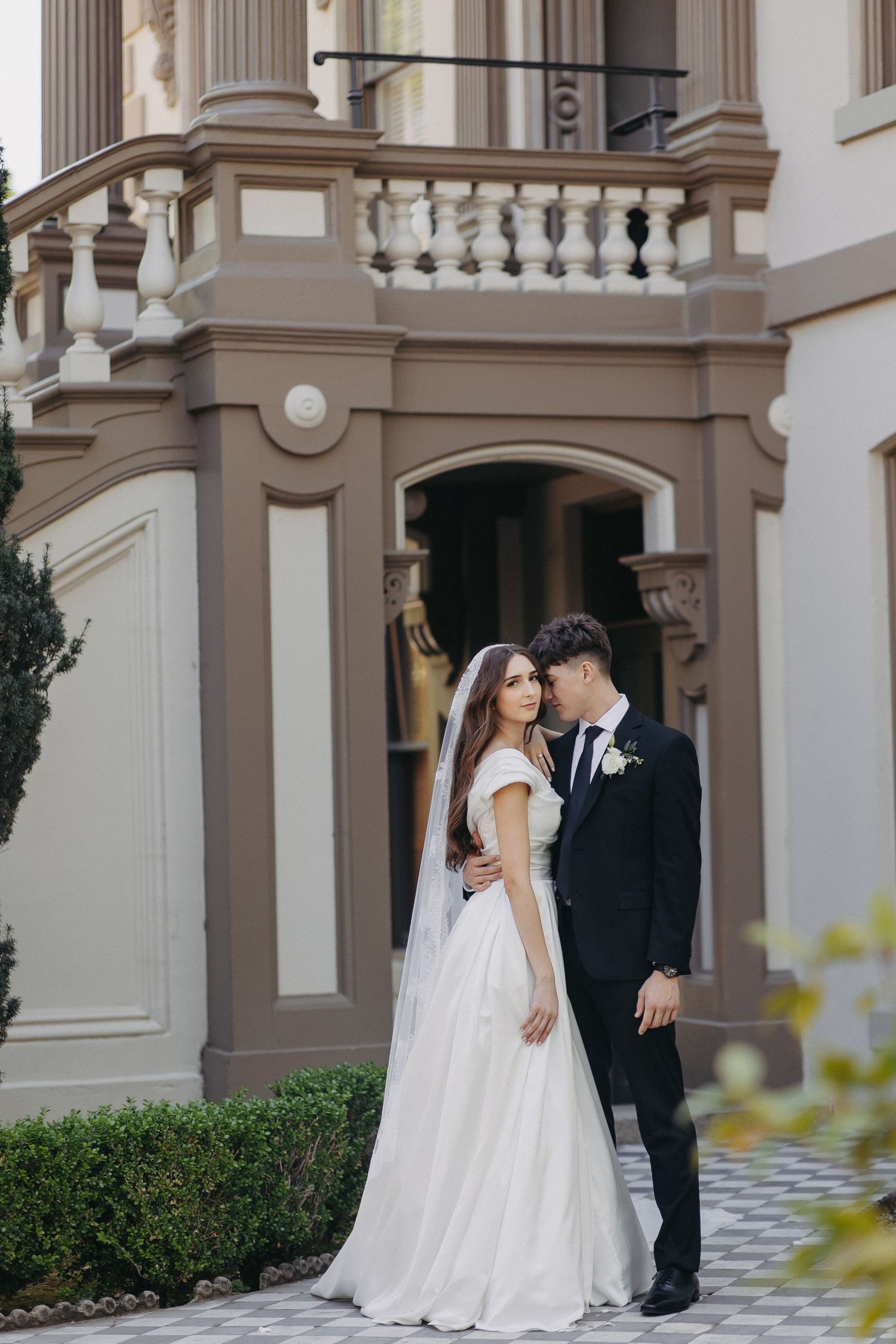 Newlyweds pose elegantly in front of a classical stone building with columns.