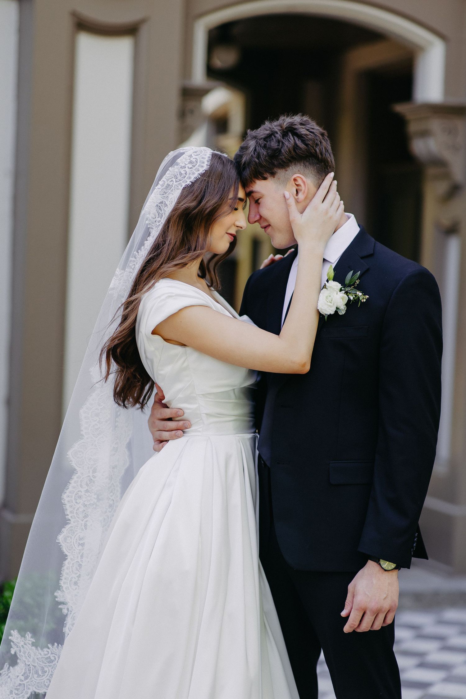 Romantic wedding portrait of a couple embracing in front of an elegant building.