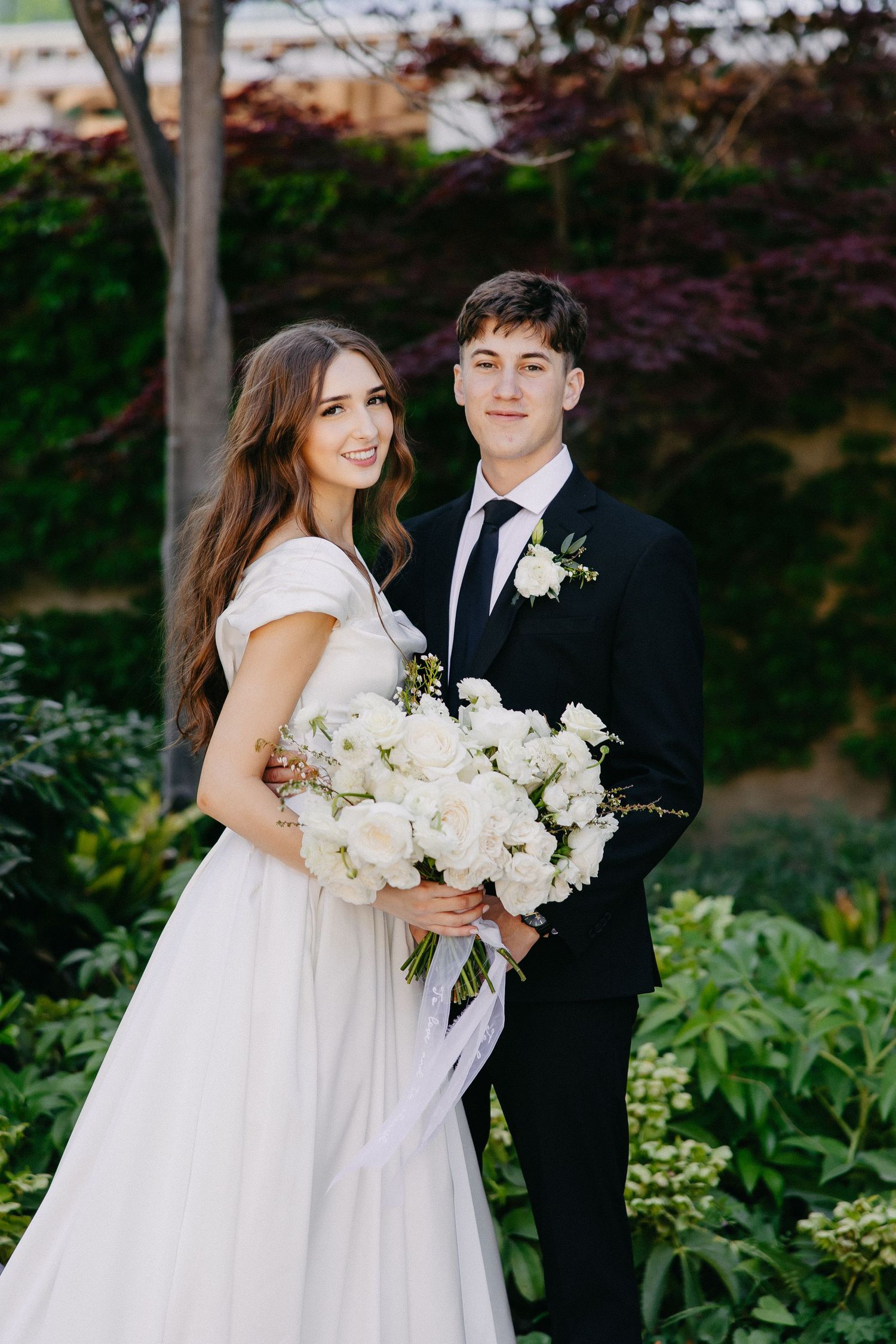 Elegant wedding portrait in a garden with white floral bouquet.