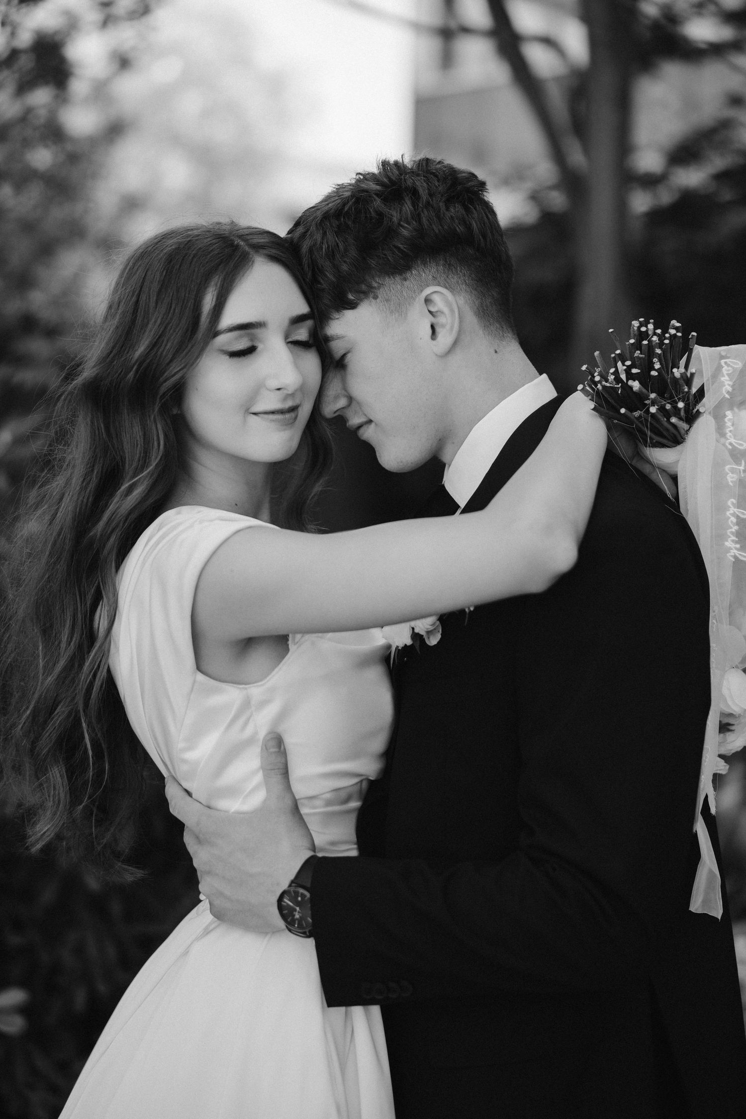 A romantic black and white portrait of newlyweds sharing a tender embrace in a garden setting.