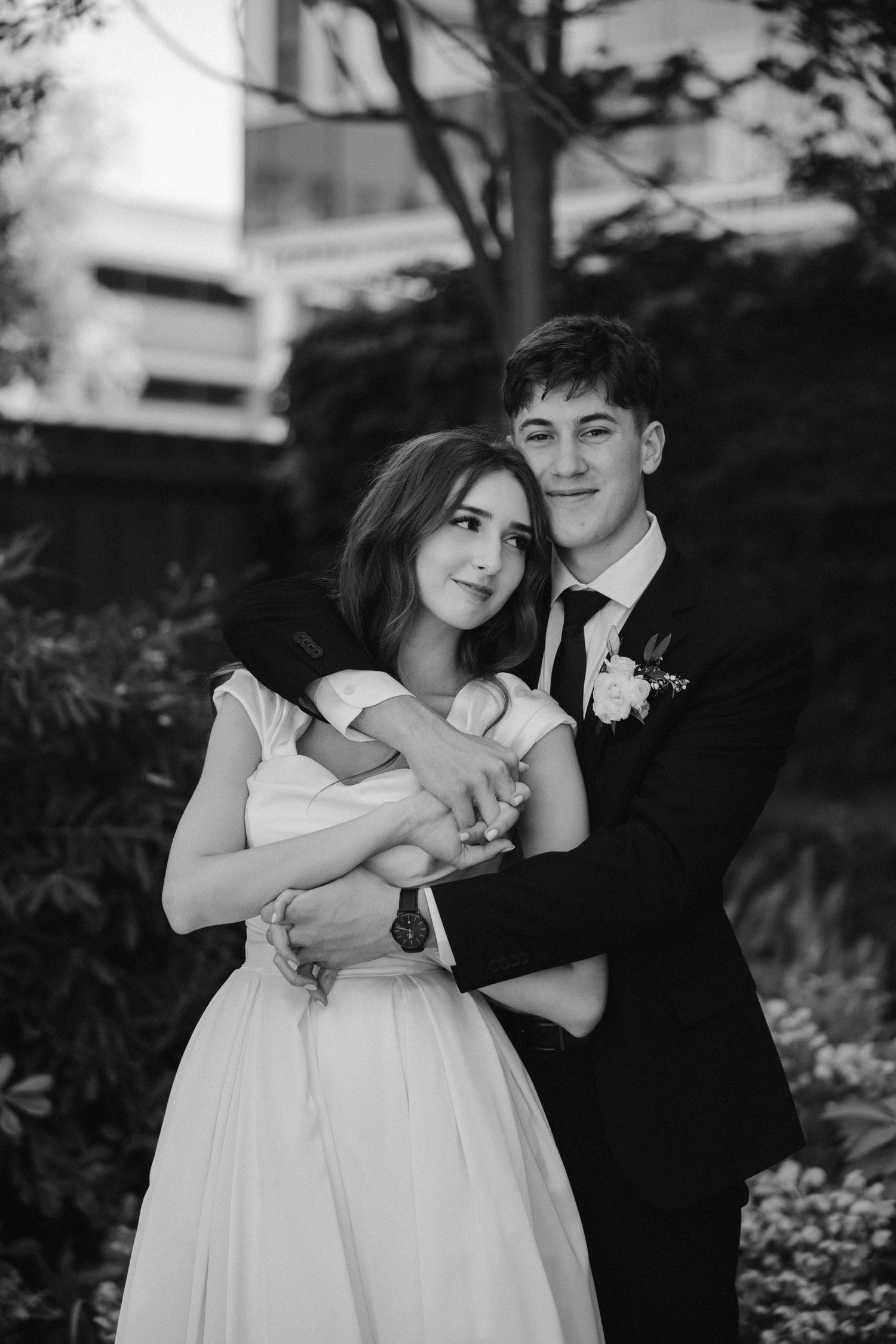 Black and white wedding portrait of a couple embracing against a natural outdoor backdrop.