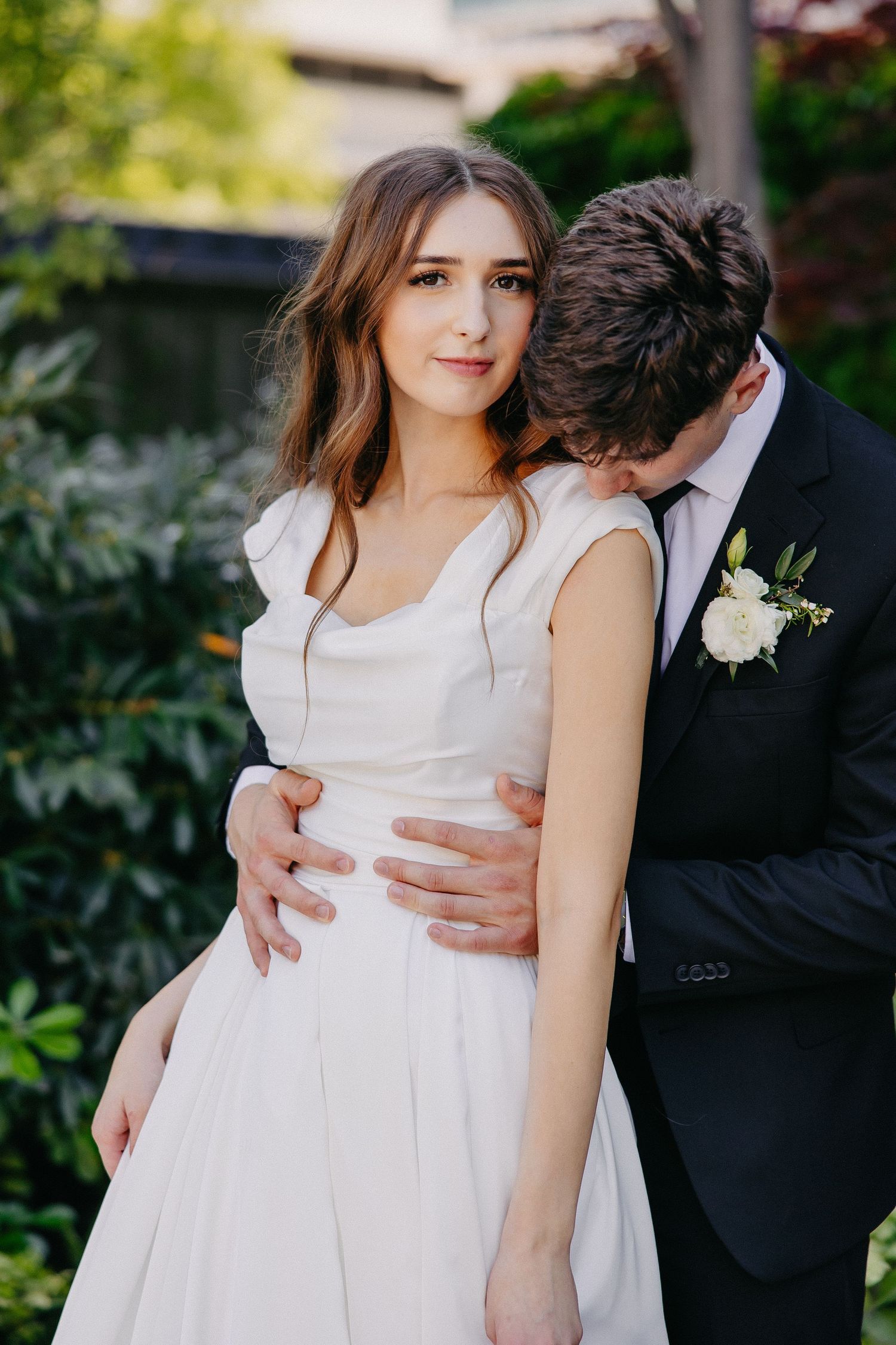 Romantic garden wedding portrait with couple in traditional white dress and black tuxedo attire.
