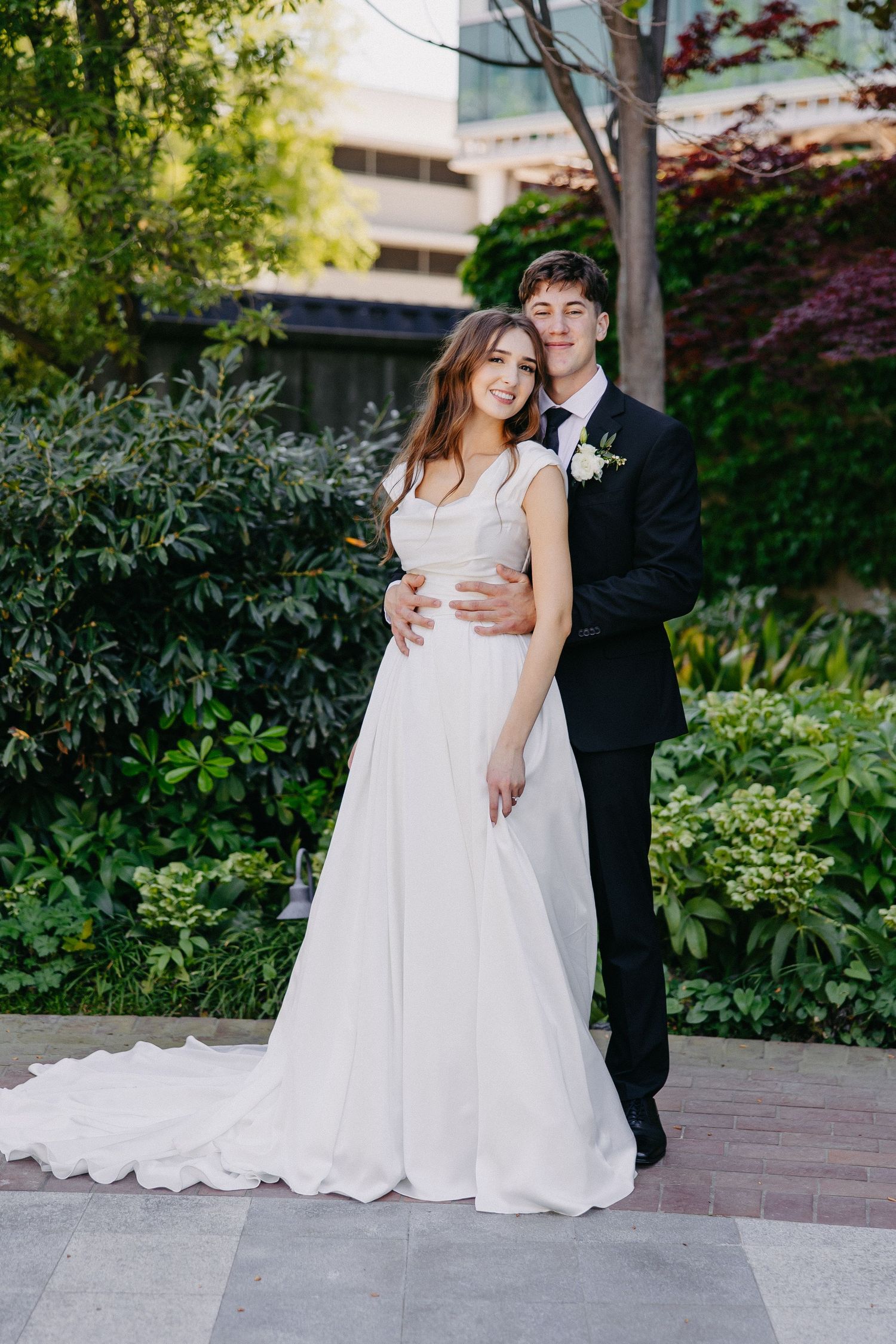 Elegant wedding portrait in a garden setting with couple in classic white gown and black suit.