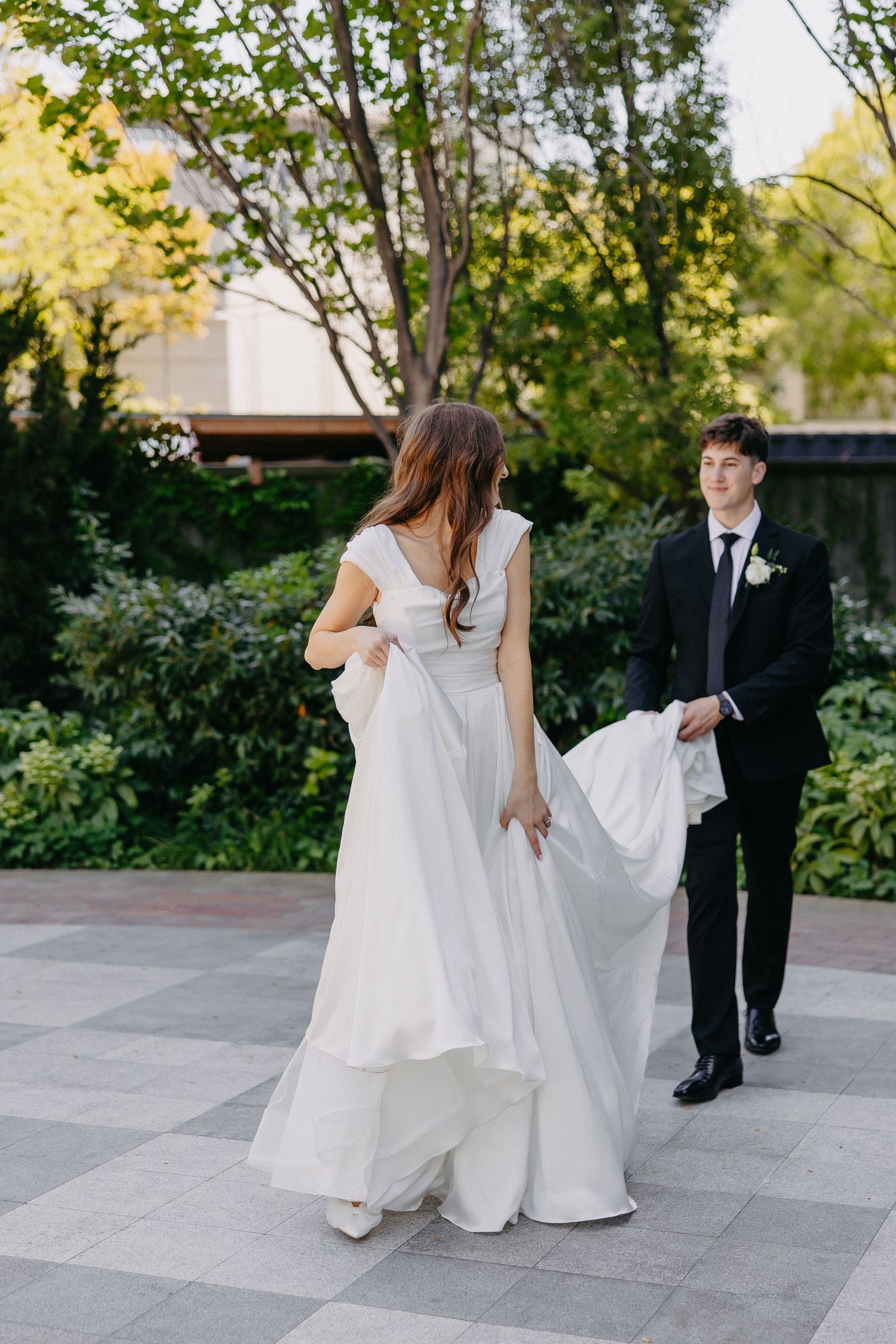 Candid wedding photo of bride showing off dress movement while groom admires from behind.