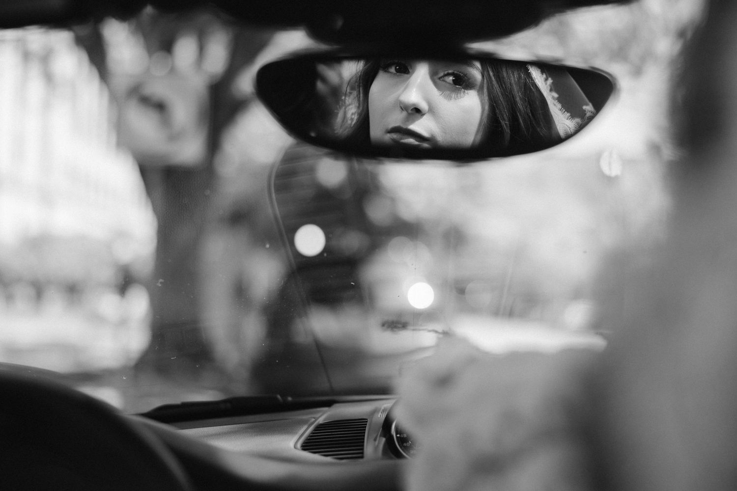 Artistic black and white reflection of bride captured in car rearview mirror.