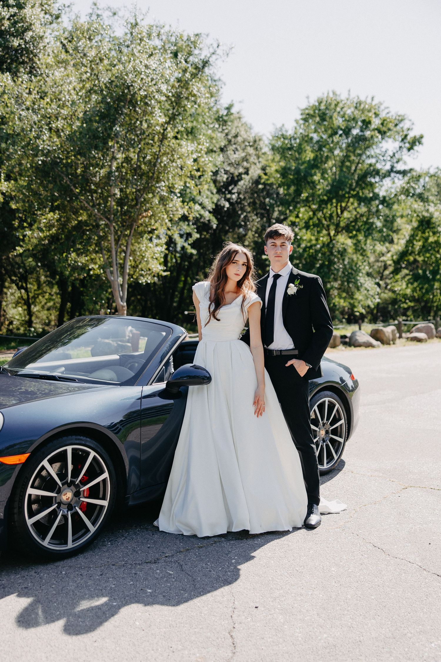 Wedding portrait with luxury Porsche 911 convertible against leafy green background.