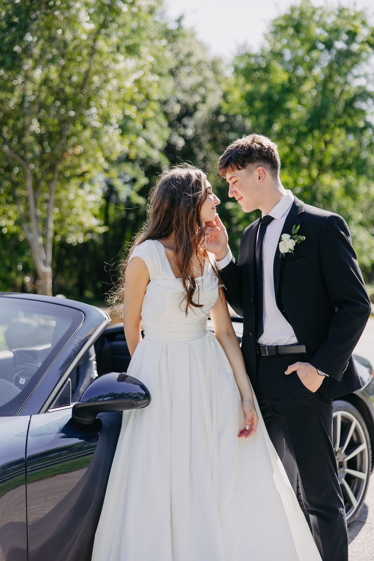 Intimate wedding portrait with couple sharing moment beside luxury Porsche convertible.