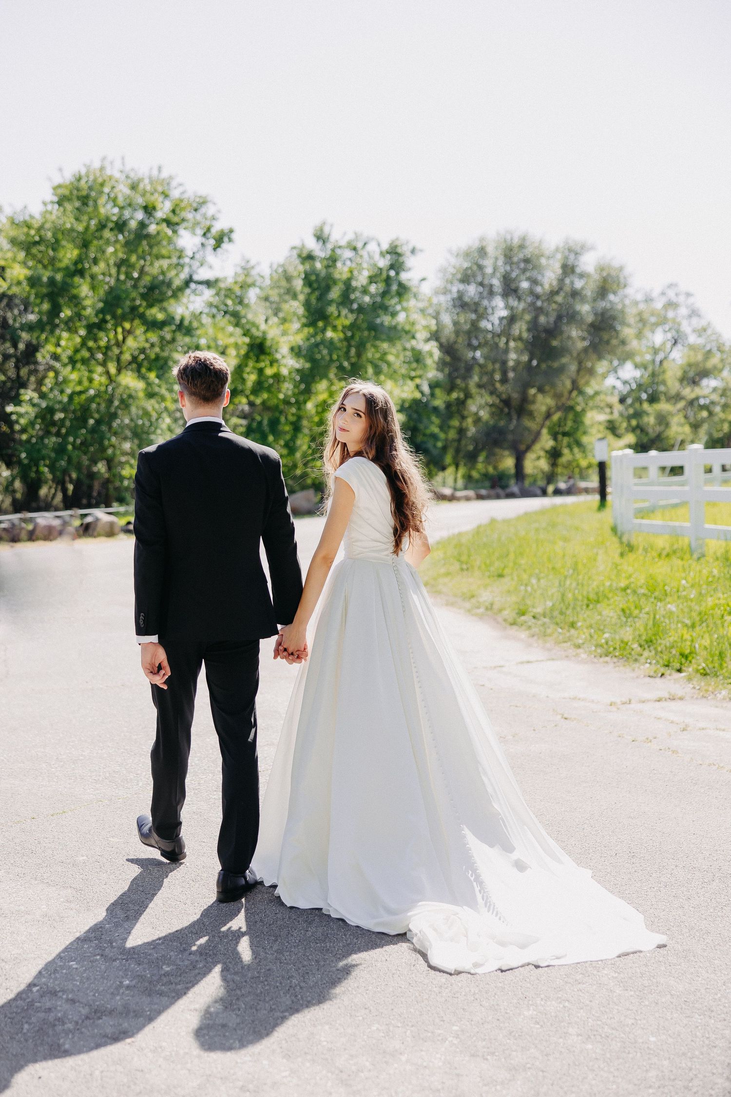 A wedding couple holding hands on a peaceful tree-lined path on their special day.