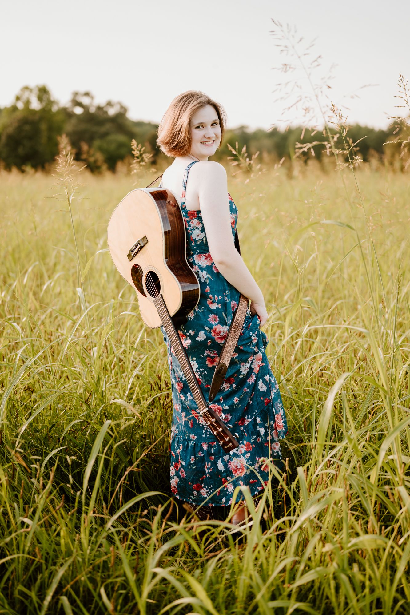 A High School Senior in a flowing magenta maxi dress poses in a grassy field with trees in the background.