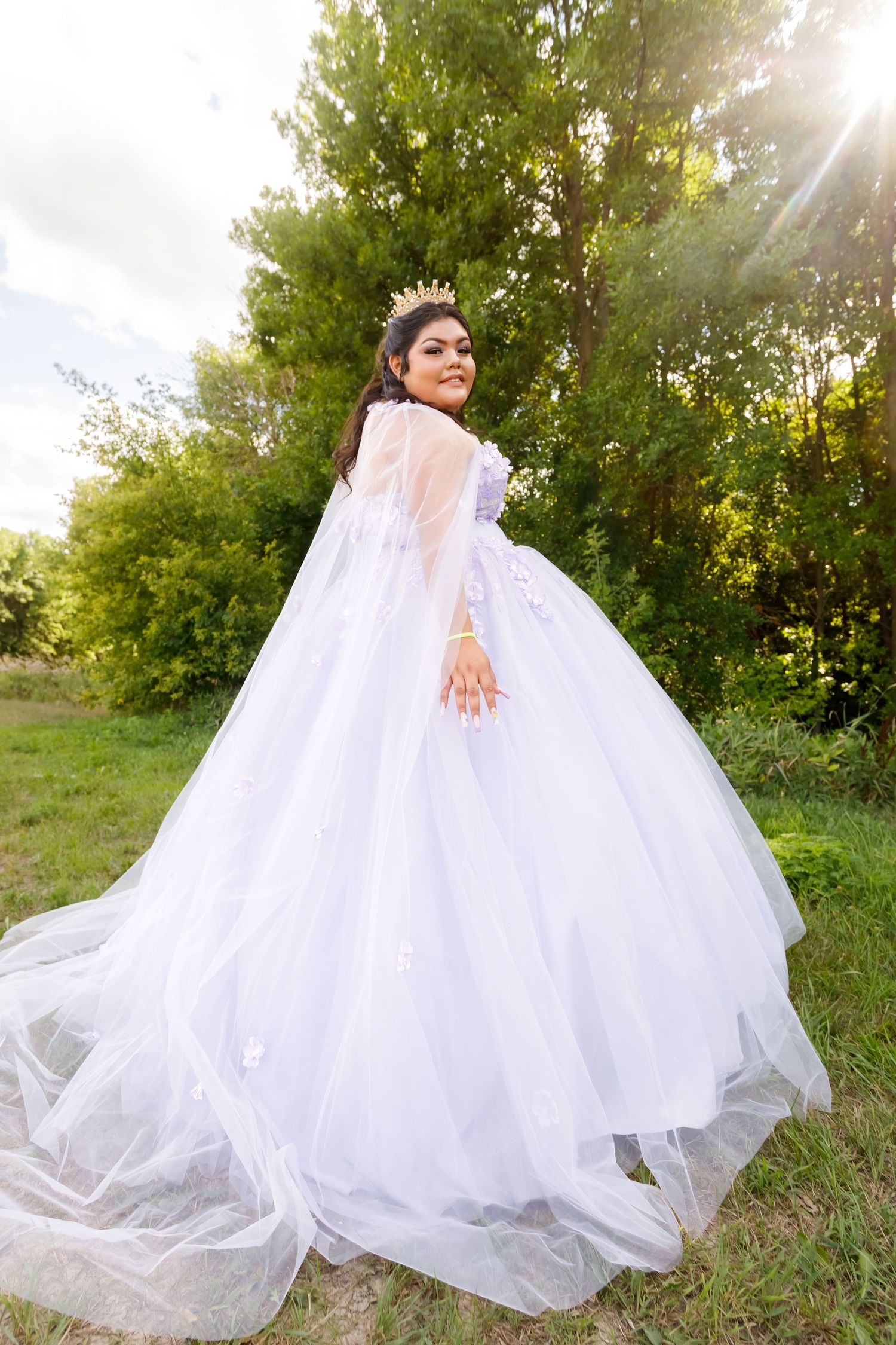 A white princess ball gown with flowing train photographed against natural greenery.