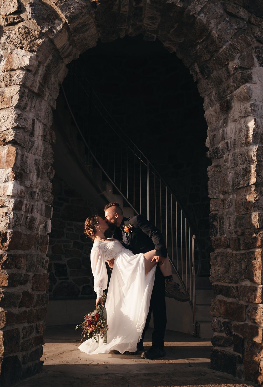 A romantic dip kiss between newlyweds in a lush garden setting.