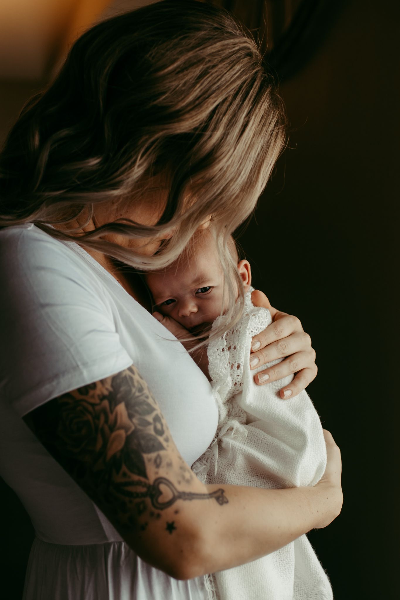 Intimate moment between parent and infant with visible arm tattoos in moody lighting.