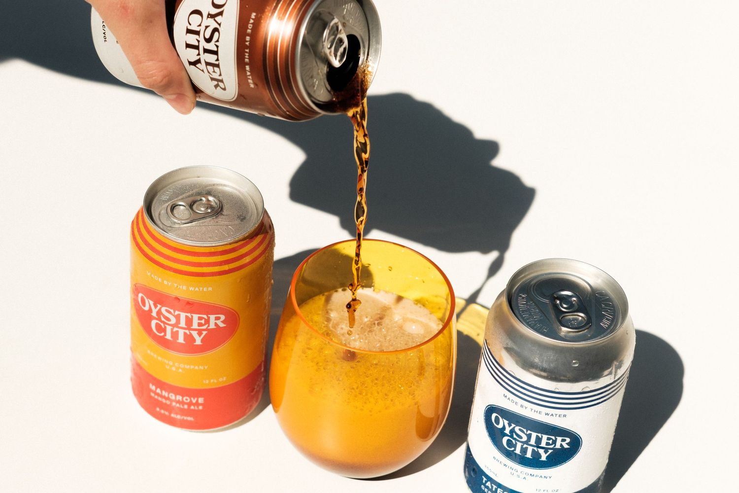 Beer cans casting shadows on a white surface with one being poured.