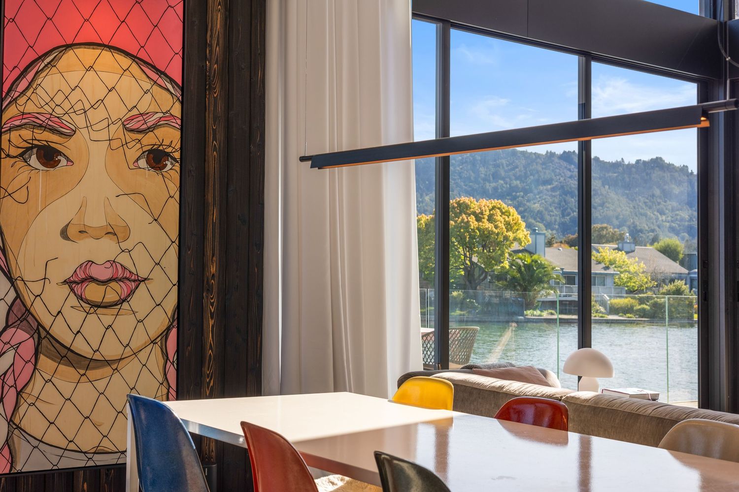 Modern restaurant interior with colorful chairs, artwork and scenic window view of mountains and water.